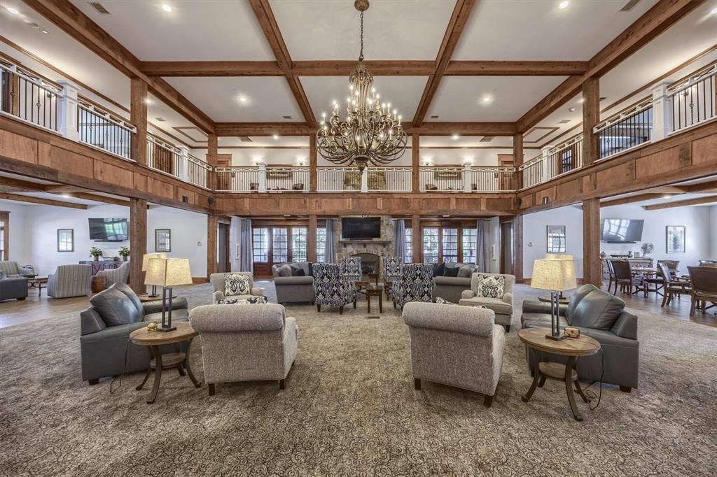Two-story great room with exposed wood beams, a prominent chandelier, stone fireplace, and multiple sets of French doors