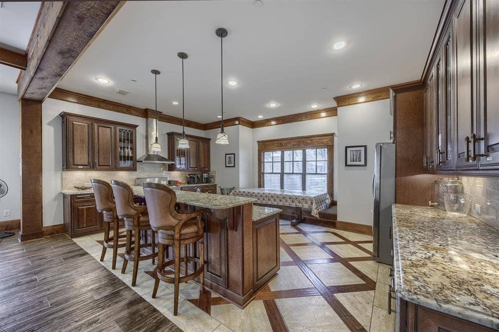 Expansive kitchen island, rich wood cabinetry, granite countertops, stainless steel range hood, and recessed lighting