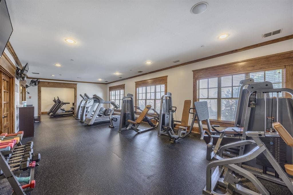 Interior fitness room featuring rubber flooring, multiple fitness machines, recessed lighting, and wood-trimmed windows