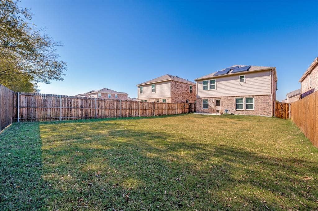 845 Poppy Cove Lane, Princeton, TX 75407 Expansive backyard with a manicured lawn, full privacy fencing, and a two-story brick and siding exterior