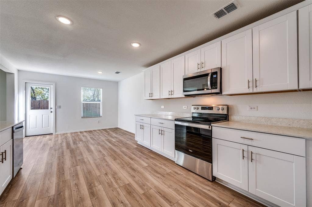 845 Poppy Cove Lane, Princeton, TX 75407 Open-concept kitchen with wood-finish flooring, white cabinetry, integrated stainless steel appliances, and light-toned countertops