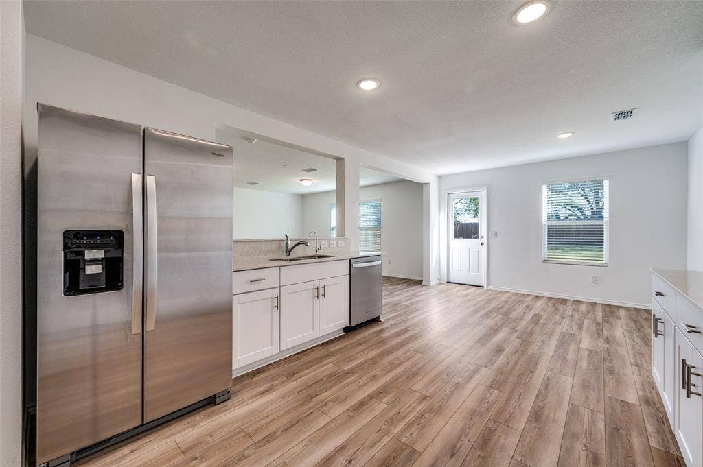 845 Poppy Cove Lane, Princeton, TX 75407 Wood-finish flooring throughout, recessed lighting, white cabinetry with silver hardware, stainless steel appliances, and a pass-through window