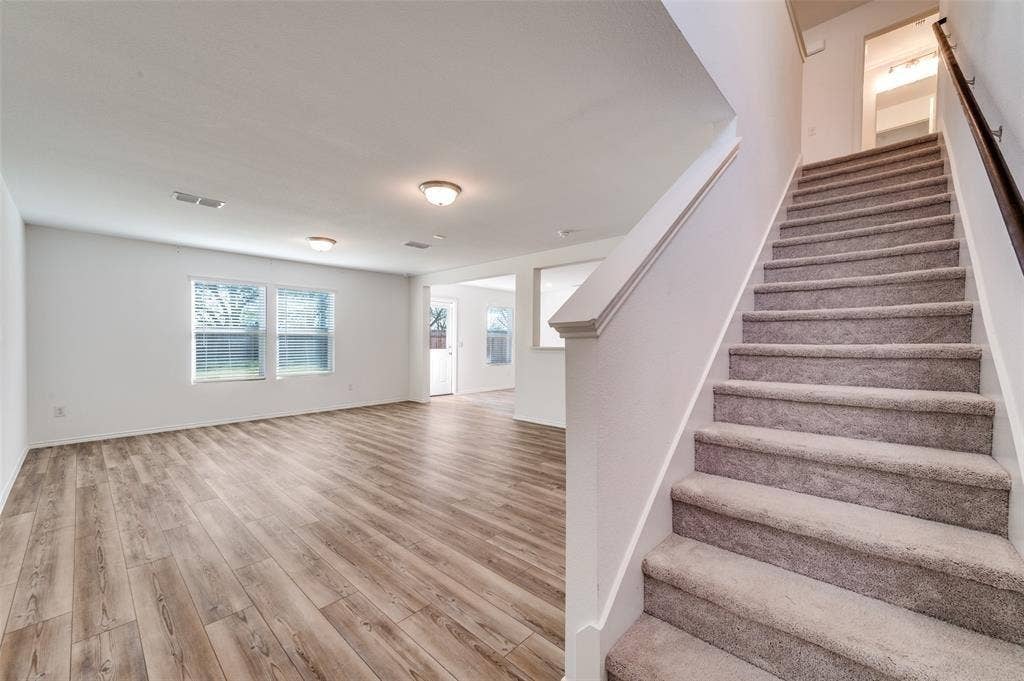 845 Poppy Cove Lane, Princeton, TX 75407 Spacious interior featuring wood-finish flooring, multiple windows, and a carpeted staircase with a dark wood handrail