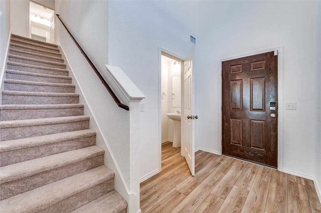 845 Poppy Cove Lane, Princeton, TX 75407 Wood-finish flooring, dark wood front door, carpeted staircase with wood handrail, and a pedestal sink in the adjacent room