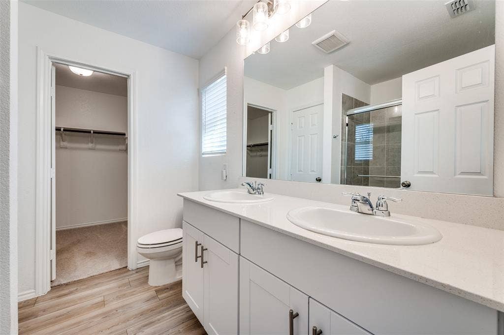 845 Poppy Cove Lane, Princeton, TX 75407 Dual vanity with white cabinetry and chrome hardware, white solid surface countertop, and wood-finish flooring