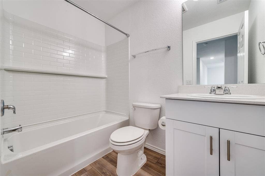 845 Poppy Cove Lane, Princeton, TX 75407 Tub and shower combination featuring subway tile surround, single vanity with integrated sink, white cabinetry with silver-tone hardware, and wood-finish flooring
