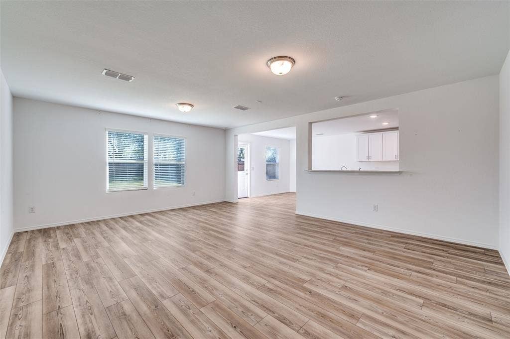 845 Poppy Cove Lane, Princeton, TX 75407 Wood-finish flooring throughout, two windows with blinds, and a pass-through opening to an adjacent room with white cabinetry