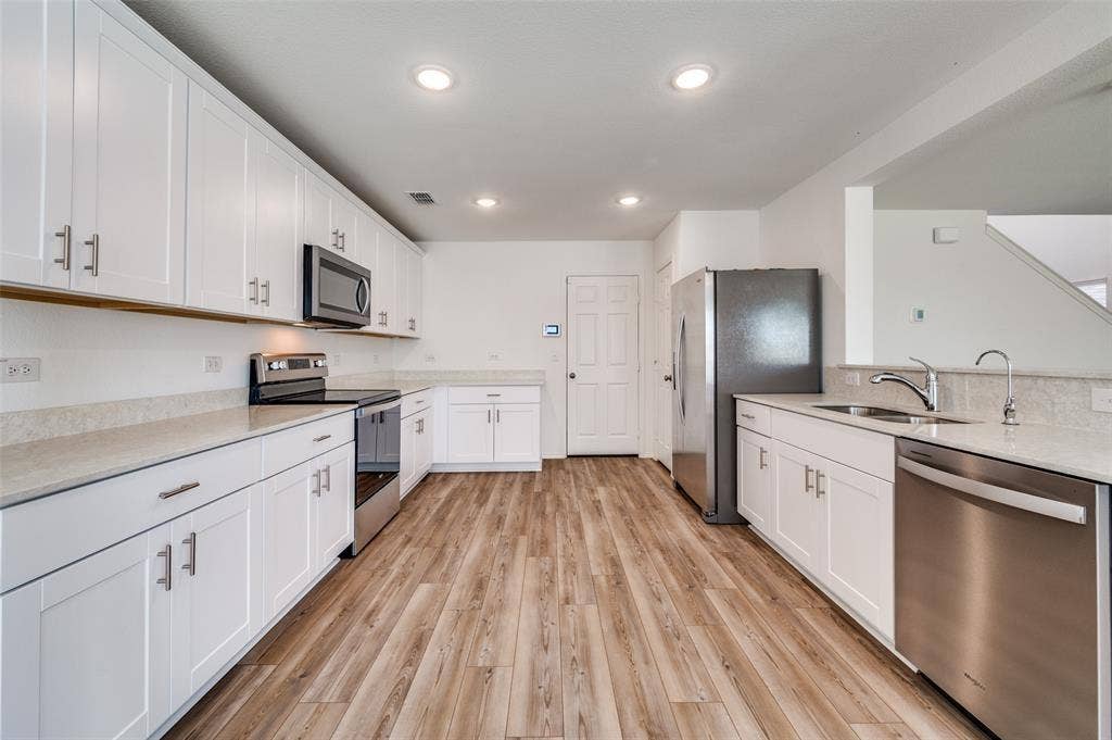 845 Poppy Cove Lane, Princeton, TX 75407 White shaker cabinetry, stainless steel appliances, wood-finish flooring, recessed lighting, and light-toned countertops