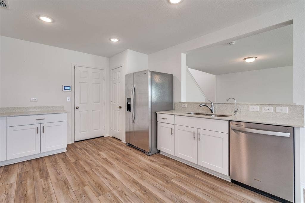 845 Poppy Cove Lane, Princeton, TX 75407 Wood-finish flooring with white cabinetry, light-toned countertops, and stainless steel appliances