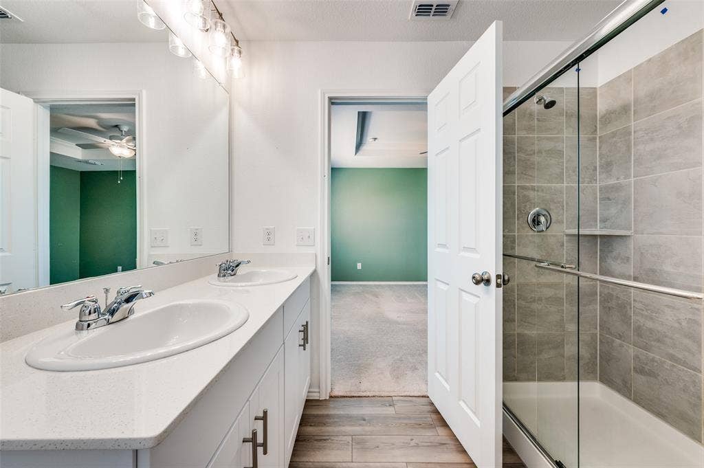 845 Poppy Cove Lane, Princeton, TX 75407 Dual vanity with white countertops, chrome fixtures, glass-enclosed shower with tile surround, and wood-finish flooring