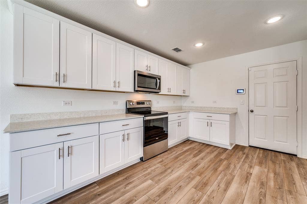 845 Poppy Cove Lane, Princeton, TX 75407 White shaker-style cabinetry with brushed nickel hardware, light-toned countertops, stainless steel appliances, and wood-finish flooring