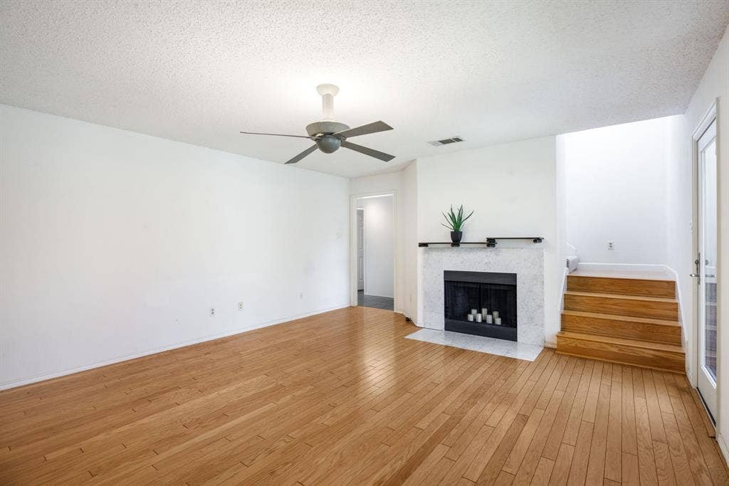 765 Eiffel Drive, Plano, TX 75023 Hardwood flooring, white painted walls, fireplace with stone surround, wood staircase, and ceiling fan