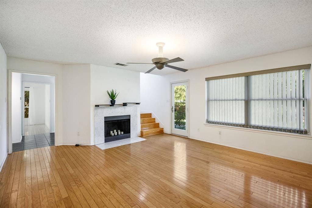 765 Eiffel Drive, Plano, TX 75023 Light wood-finish flooring, a white-framed window with vertical blinds, a ceiling fan, and a fireplace with a white surround