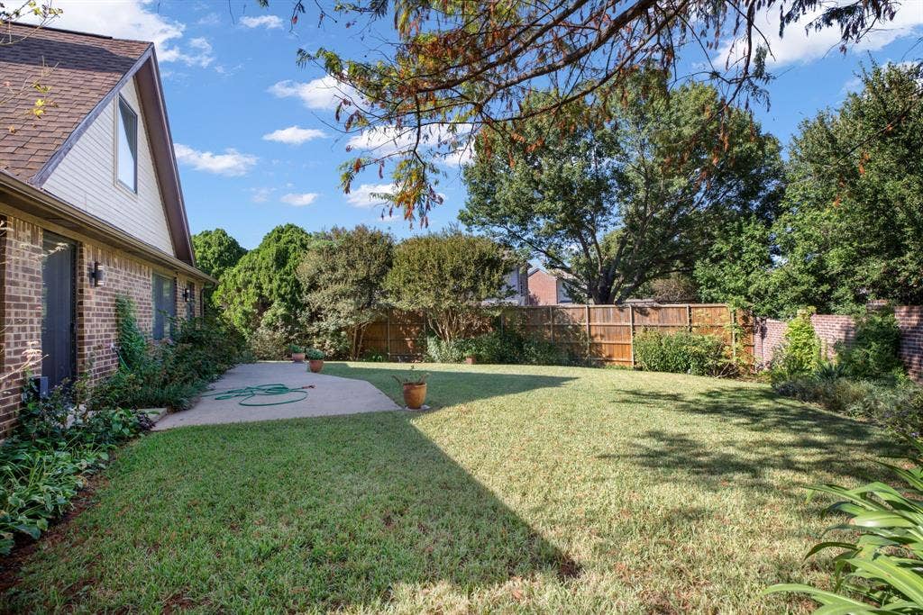 765 Eiffel Drive, Plano, TX 75023 Expansive backyard featuring a manicured lawn, concrete patio, mature trees, and a combination wood and brick privacy fence