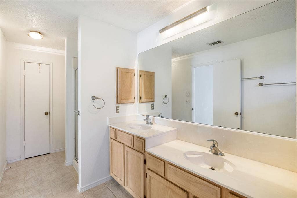 765 Eiffel Drive, Plano, TX 75023 Dual vanity with light wood-finish cabinetry and integrated sinks, complemented by a large wall-mounted mirror