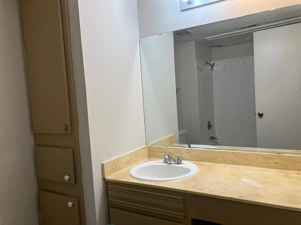 5727 Harvest Hill Road, #1042, Dallas, TX 75230 Vanity with integrated sink, expansive mirrored wall, built-in storage cabinetry, and shower with tile surround