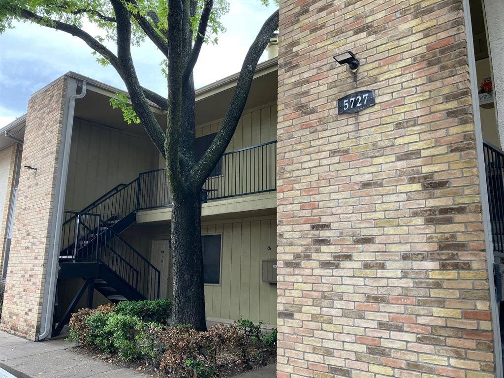 5727 Harvest Hill Road, #1042, Dallas, TX 75230 Building exterior featuring multi-toned brick facade, black metal railings, and a prominent address number