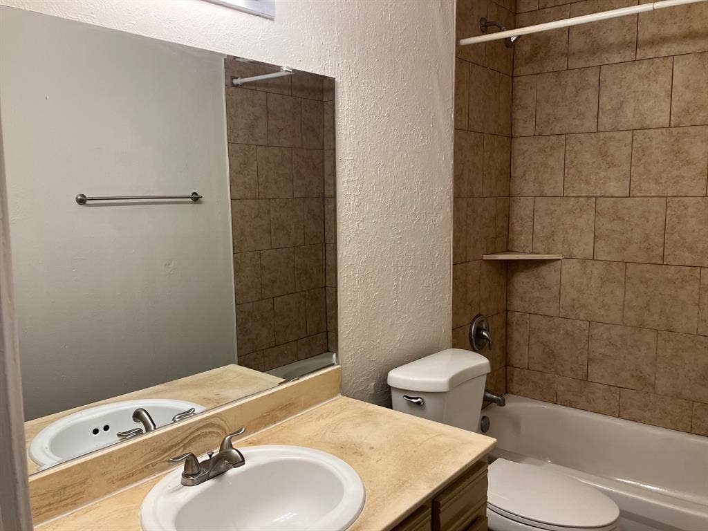 5727 Harvest Hill Road, #1042, Dallas, TX 75230 Bathroom featuring a vanity with a drop-in sink, a built-in mirror, a toilet, a bathtub with a shower, and tile surround