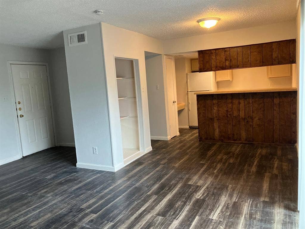 5727 Harvest Hill Road, #1042, Dallas, TX 75230 Wood-finish flooring throughout, built-in shelving, white paneled entry door, and a kitchen pass-through with wood paneling