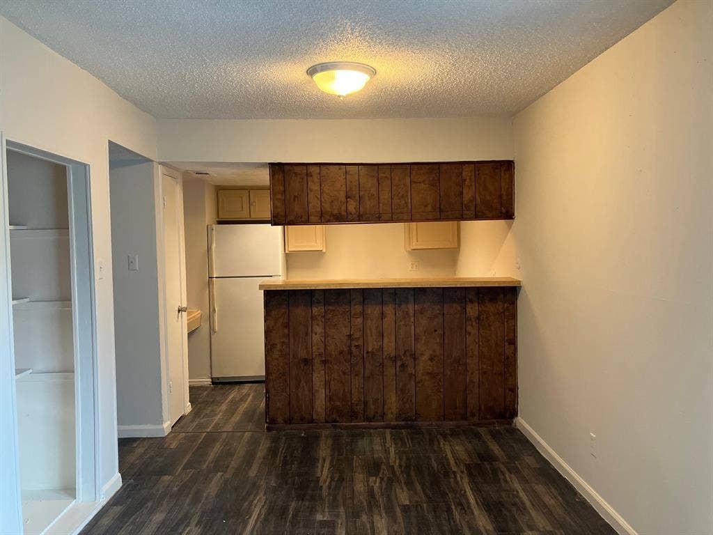 5727 Harvest Hill Road, #1042, Dallas, TX 75230 Wood-finish flooring, built-in shelving, wood-paneled breakfast bar, overhead lighting, and a refrigerator