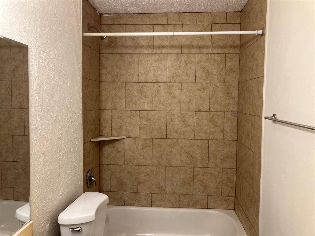5727 Harvest Hill Road, #1042, Dallas, TX 75230 Built-in bathtub with subway tile surround, integrated corner shelf, and wall-mounted shower fixtures
