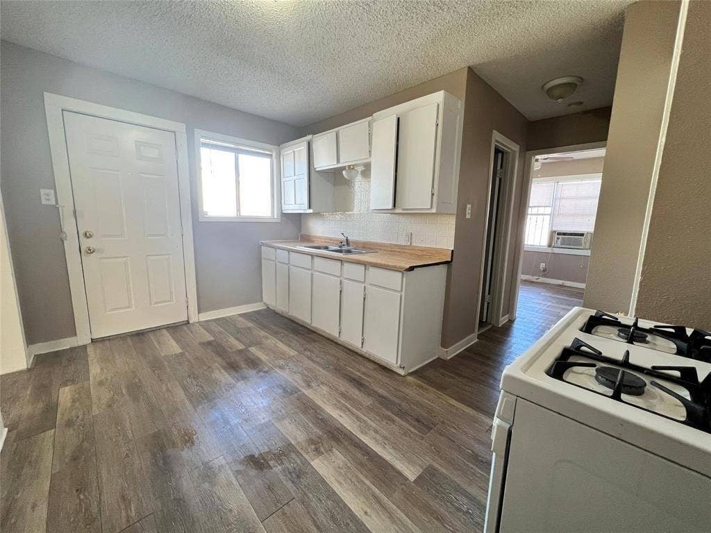 2745 S Jones Street, Fort Worth, TX 76104 Kitchen featuring wood-finish flooring, white cabinetry, a window for natural light, and a built-in range