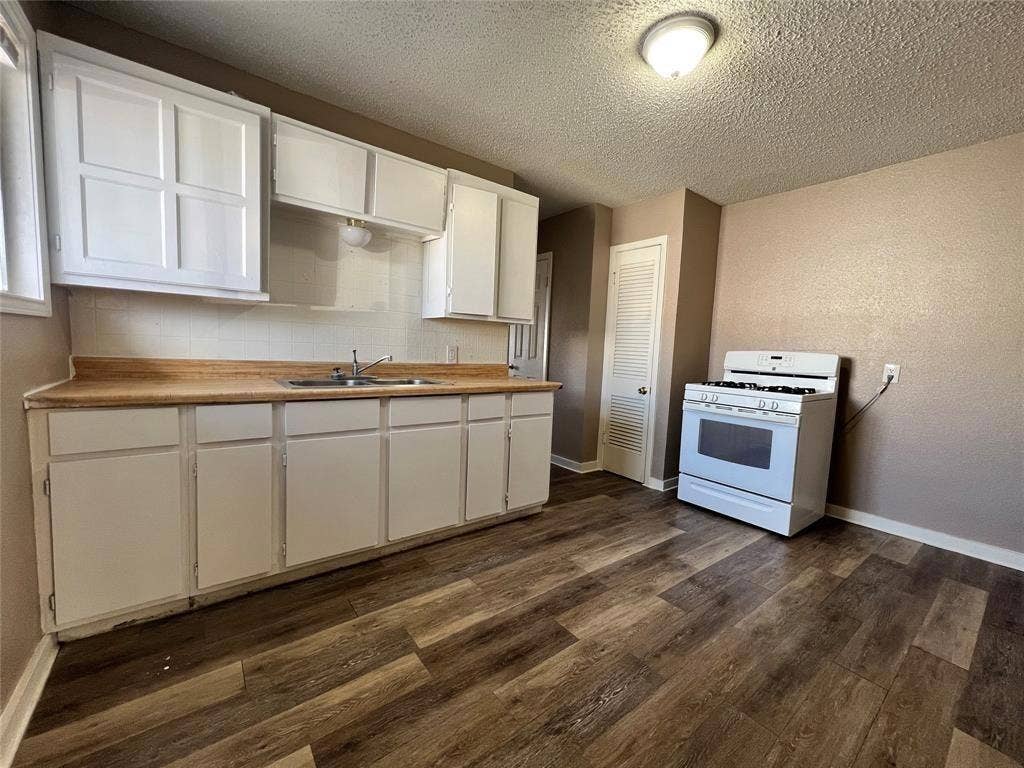 2745 S Jones Street, Fort Worth, TX 76104 Kitchen featuring wood-finish flooring, white cabinetry, a white gas range, and a dual-basin sink with a wood-finish countertop