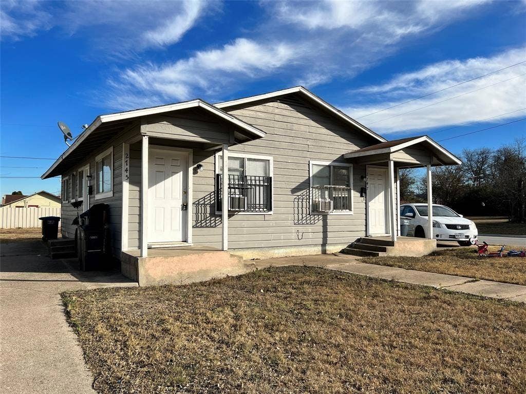 2745 S Jones Street, Fort Worth, TX 76104 Single-story residence featuring light gray siding, white entry doors, and a concrete pathway