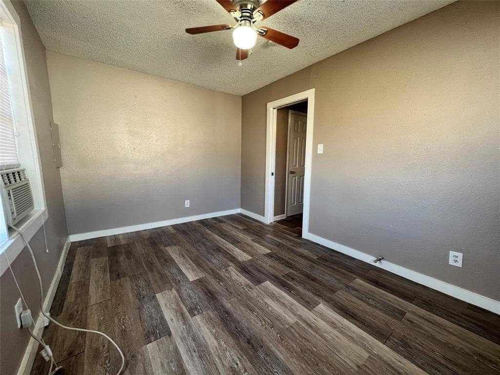 2745 S Jones Street, Fort Worth, TX 76104 Wood-finish flooring, ceiling fan with integrated lighting, neutral wall paint, white trim, and a window-mounted air conditioning unit