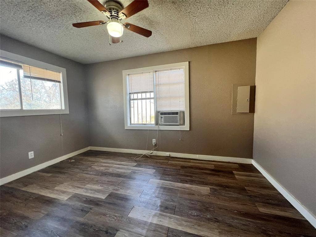 2745 S Jones Street, Fort Worth, TX 76104 Wood-finish flooring, ceiling fan with integrated lighting, window-mounted air conditioning unit, and multiple windows