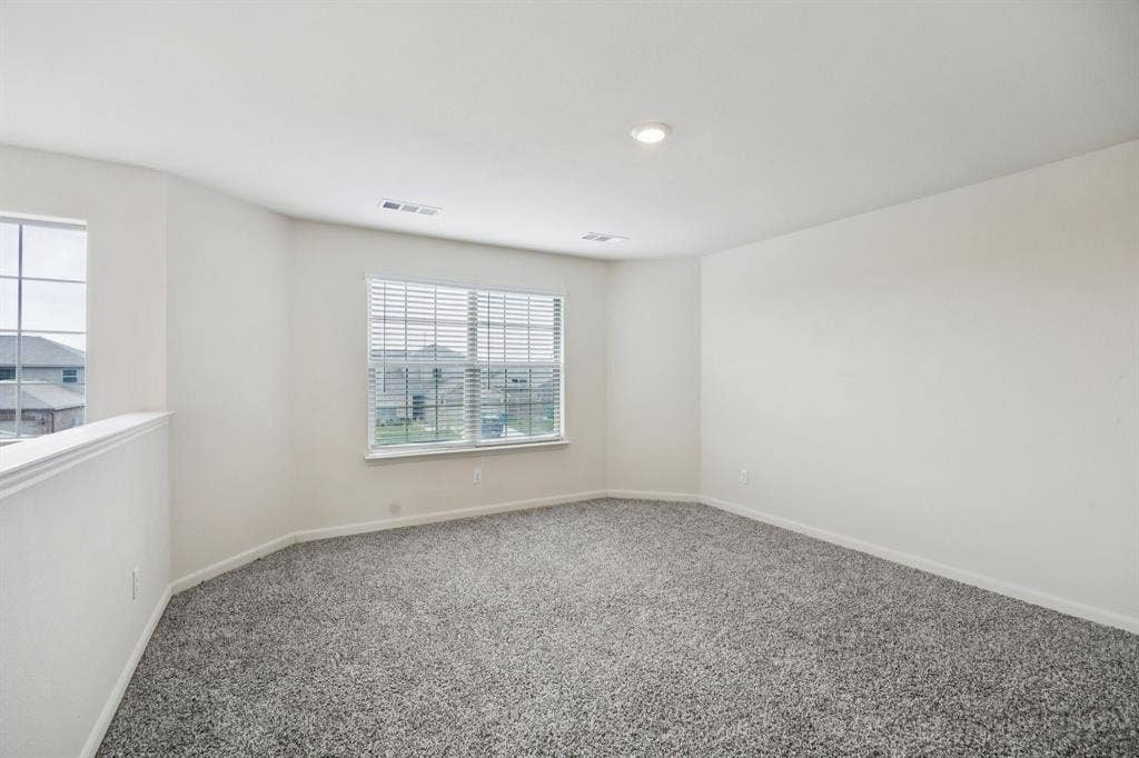 Expansive carpeted area featuring two windows with blinds, a half-wall partition, and recessed ceiling lighting