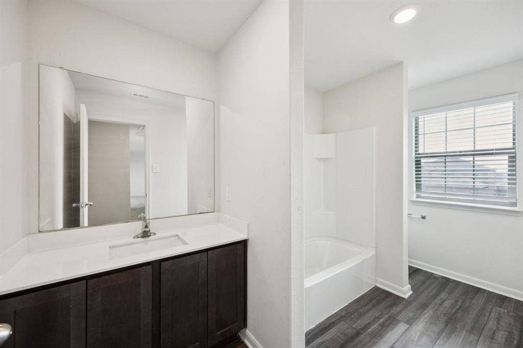 Bathroom featuring a dark wood-finish vanity with a white countertop, an integrated rectangular sink, a large wall-mounted mirror, and wood-finish flooring