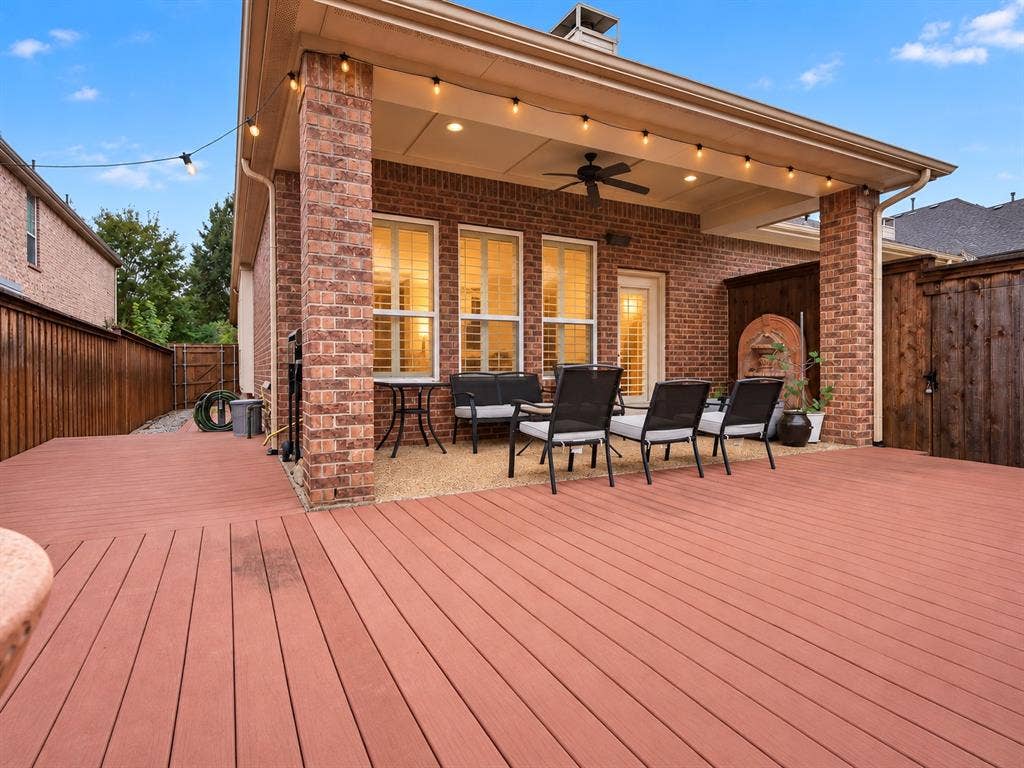 Expansive wood-finish deck with a covered patio featuring a ceiling fan, recessed lighting, and brick columns