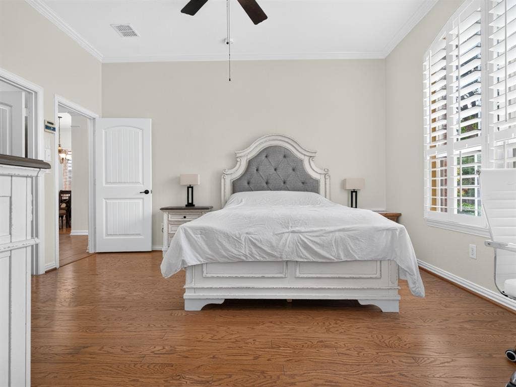 Wood-finish flooring throughout, arched window with plantation shutters, ceiling fan, and crown molding
