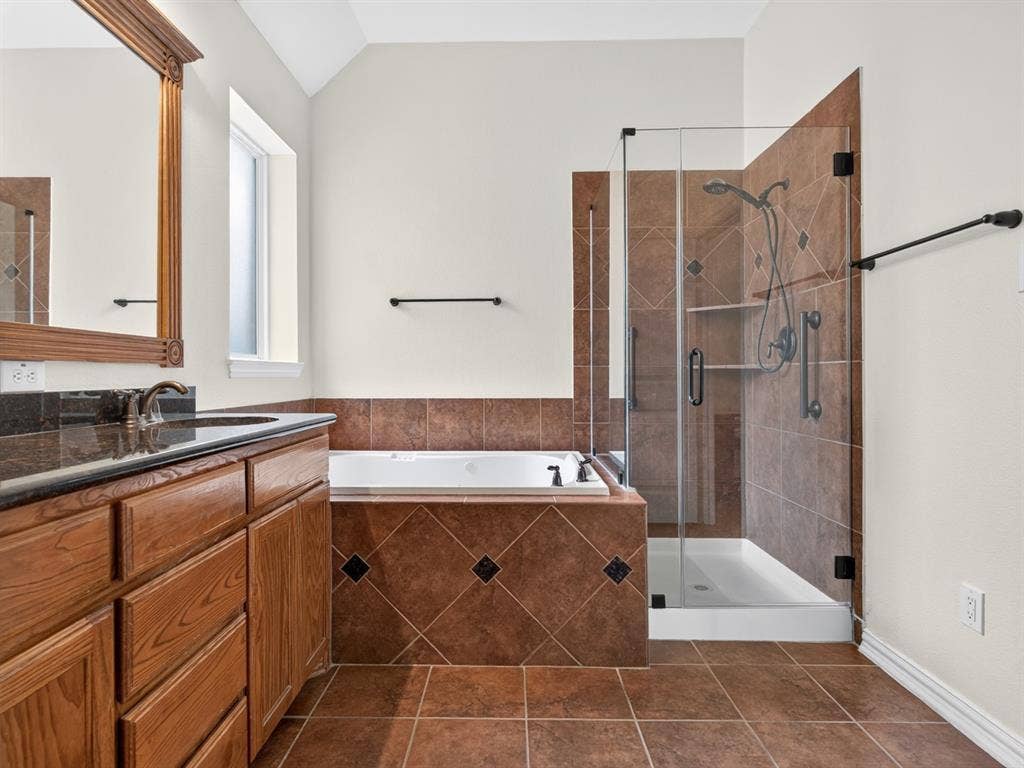 Spacious bathroom featuring a wood vanity with a dark countertop, an integrated soaking tub, a separate glass-enclosed shower, and tile flooring