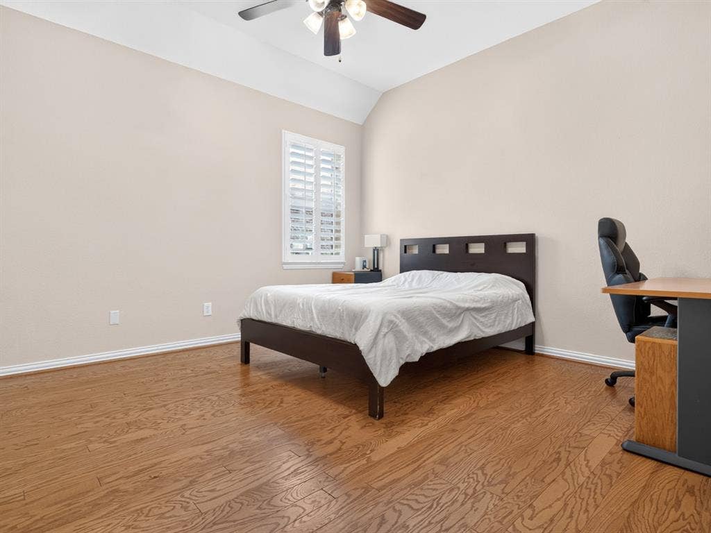 Vaulted ceiling, wood-finish flooring, white plantation shutters, and a ceiling fan with integrated lighting