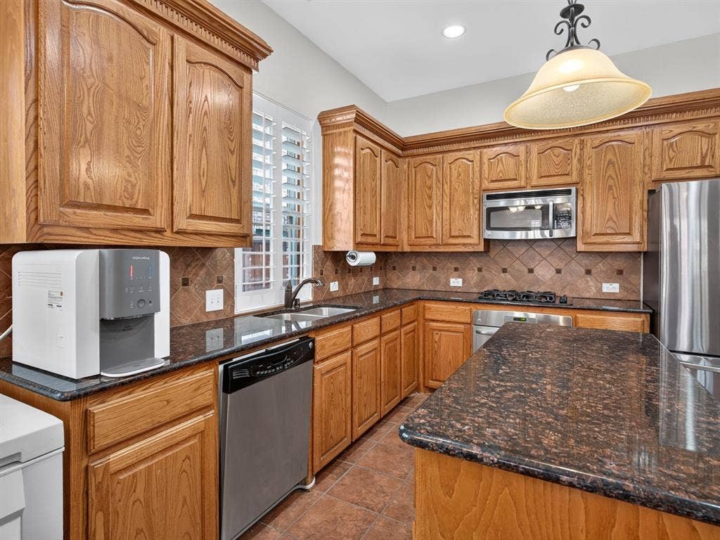 Wood-finish cabinetry with crown molding, dark speckled countertops, stainless steel appliances, and a tiled backsplash