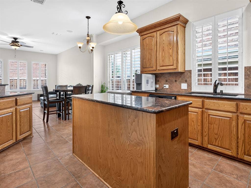 Kitchen featuring a central island, wood cabinetry, granite countertops, tile flooring, and plantation shutters