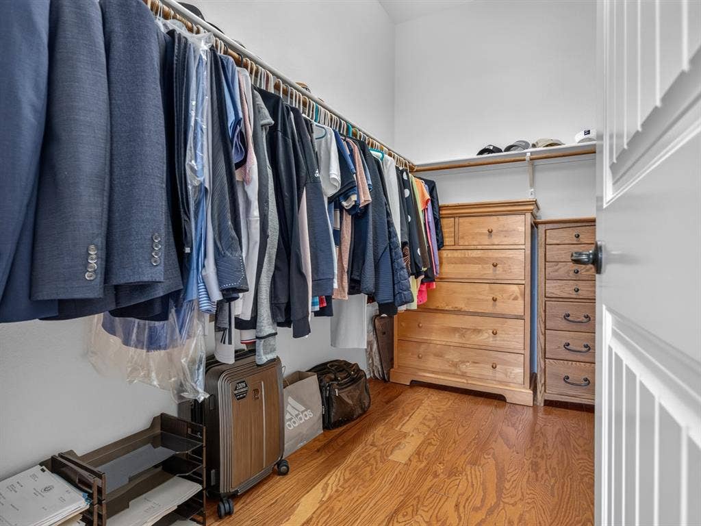 Walk-in closet featuring wood-finish flooring, white walls, and built-in shelving