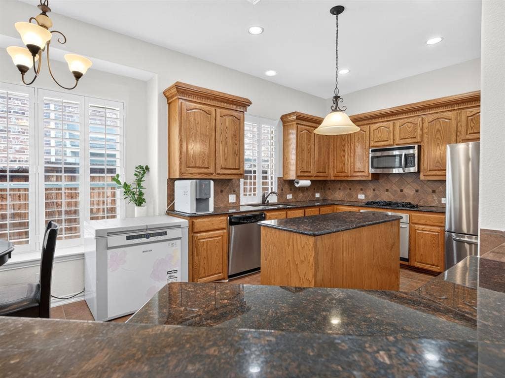 Kitchen featuring a central island, wood cabinetry, dark countertops, stainless steel appliances, and window shutters