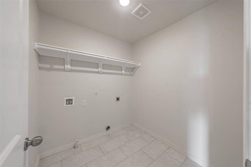 6215 Roby Drive, Arlington, TX 76001 Washroom with washer hookup, electric dryer hookup, light tile patterned floors. Long shelve for storage and rod to hang clothing.