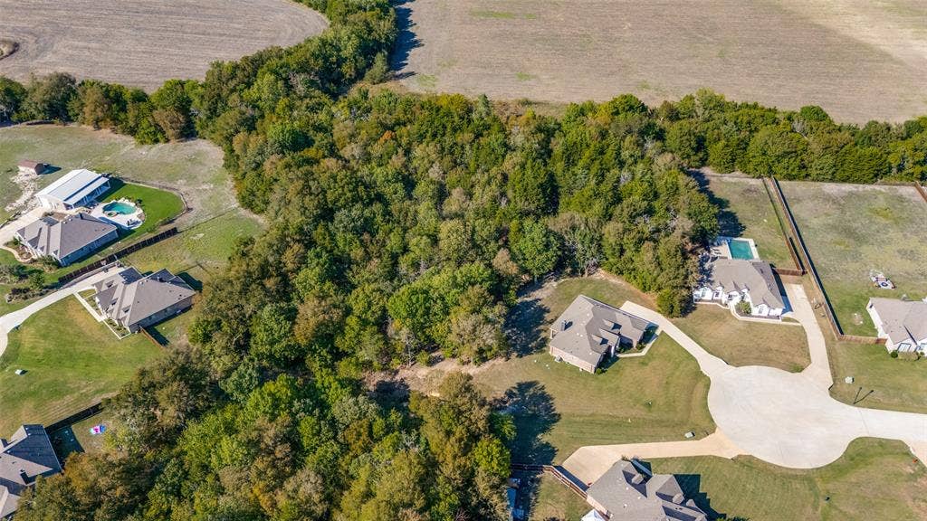 Expansive land parcel featuring mature trees, surrounding properties, and a paved street