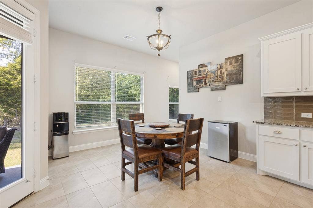 White cabinetry, stone-finish countertops, tiled backsplash, large windows, and tiled flooring