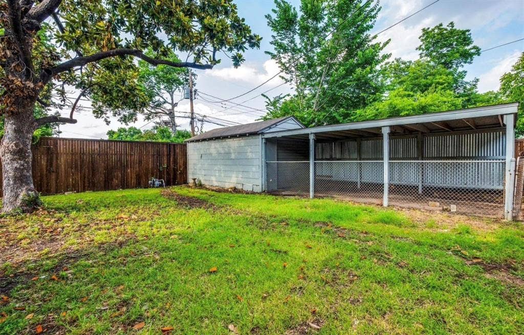 Expansive backyard featuring a wood privacy fence, mature trees, and a covered outbuilding with corrugated metal siding and chain-link fencing