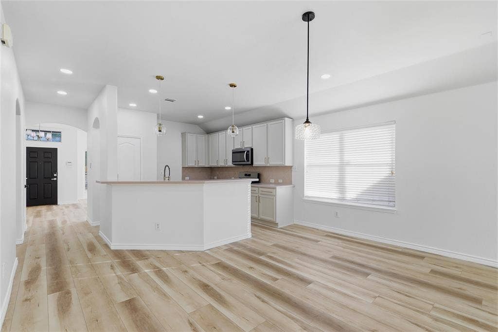 10709 Nantucket Drive, Rowlett, TX 75089 Wood-finish flooring, recessed lighting, sleek pendant lights, light-toned cabinetry, and stainless steel appliances