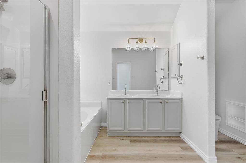 10709 Nantucket Drive, Rowlett, TX 75089 Dual sink vanity with light gray cabinetry, wall-mounted mirror, and gold-finish vanity lighting
