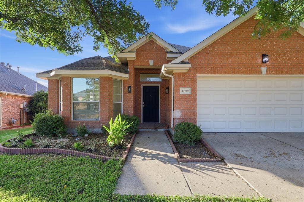 10709 Nantucket Drive, Rowlett, TX 75089 Brick facade with a white garage door, concrete walkway, and landscaped front garden