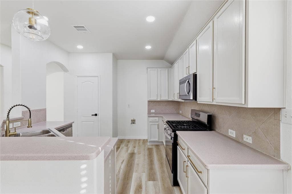 10709 Nantucket Drive, Rowlett, TX 75089 Modern kitchen featuring light wood-finish flooring, white cabinetry with gold-tone hardware, a stainless steel microwave, and a black gas range