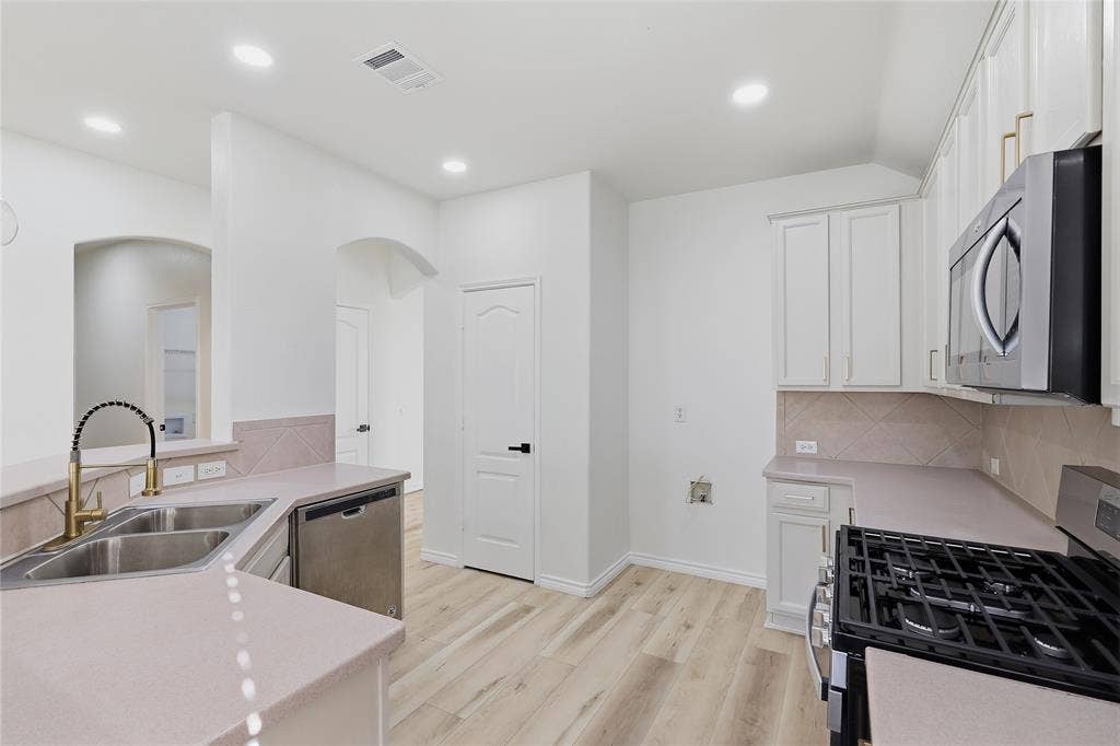 10709 Nantucket Drive, Rowlett, TX 75089 Kitchen featuring wood-finish flooring, recessed lighting, white cabinetry, a stainless steel gas range, and a dual basin sink with a gold-finish faucet