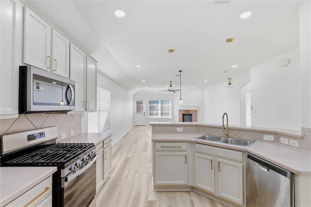 10709 Nantucket Drive, Rowlett, TX 75089 Light-toned kitchen cabinetry with gold-finish hardware, stainless steel appliances, and a double basin sink
